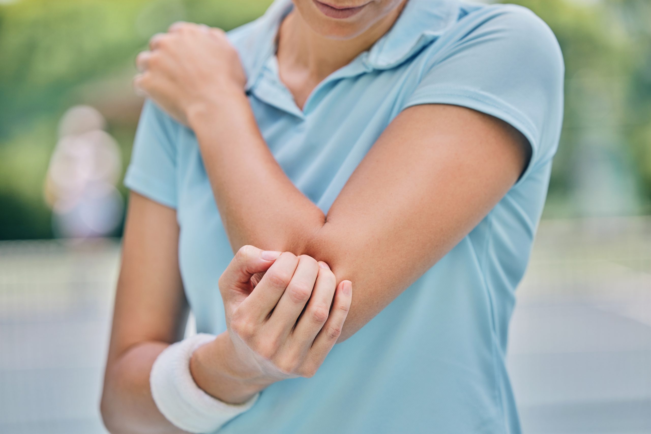 Woman in light blue shirt holding her elbow with visible discomfort or pain